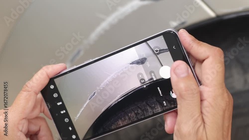 Female car insurance officer's hand uses smartphone take photo scratched wheel arch and damage from collision with concrete wall as evidence for a car insurance claim at a service center.