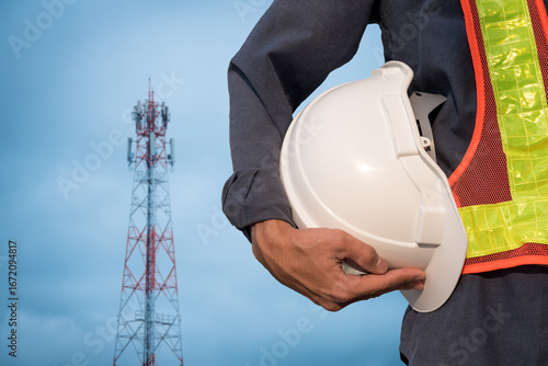 Communication engineer holding a white hard hat against a blue sky background
