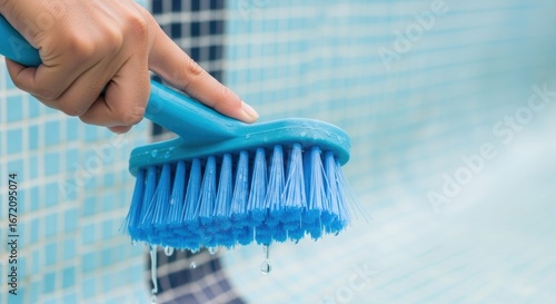Hand cleaning swimming pool tiles with blue brush