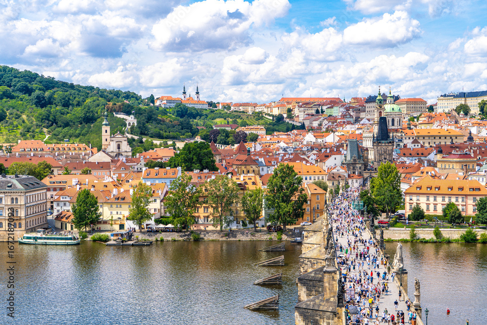 Fototapeta premium Prague from above the historic quarters of Mala Strana, Charles Bridge, and the calm waters of the Vltava River framed by summer greenery and a blue sky.Prague,Czech Republic