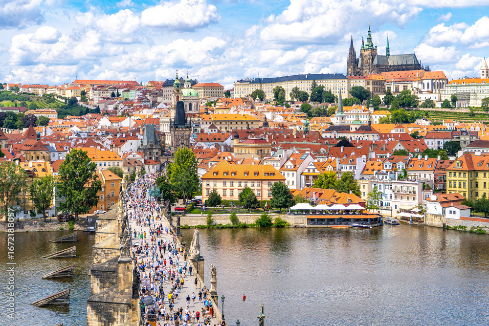 Obraz premium Prague from above the historic quarters of Mala Strana, Charles Bridge, Prague Castle, and the calm waters of the Vltava River framed by summer greenery and a blue sky.Prague,Czech Republic.