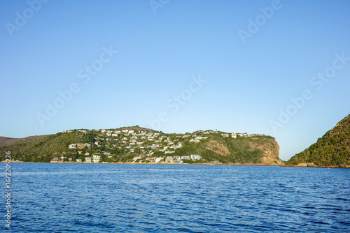 Beautiful cliffside community with houses built along green hills and rocky slopes overlooking the calm blue ocean. A stunning coastal landscape perfect for themes of travel, lifestyle, real estate
