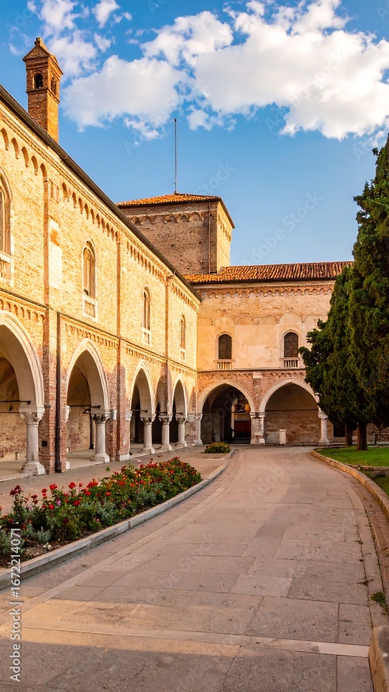 Obraz premium A sun-drenched courtyard of a historic building, showcasing arches, stonework, and landscaping.