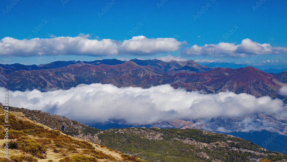 Naklejka premium Layered Mountain Landscape Under Blue Sky with White Clouds
