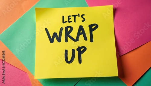 Yellow sticky note with bold black text LETS WRAP UP rests on colorful layered paper sheets. Message suggests finishing task event. Clean background highlights communication memo for business