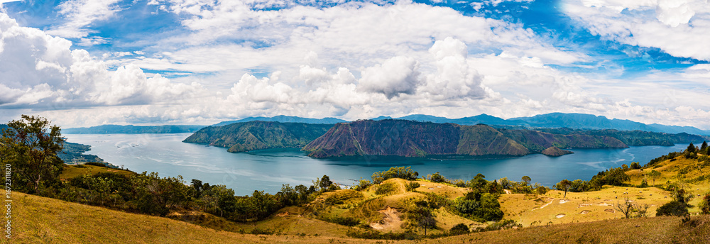 Obraz premium Panoramic view of Lake Toba from Sibea-bea Hill in Samosir, North Sumatra, Indonesia. The breathtaking landscape features the vast volcanic lake surrounded by lush green hills and mountains, showcasin