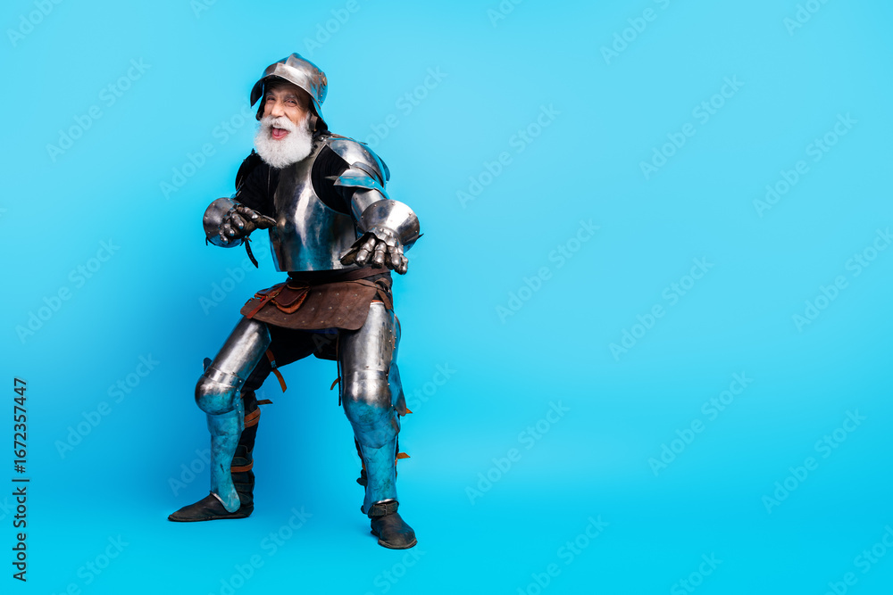 Naklejka premium Elderly man in shiny medieval knight armor posing on light blue background