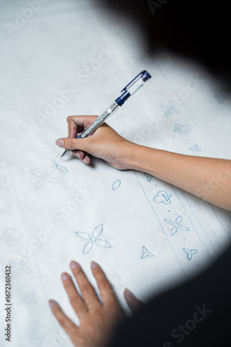 Hand drawing batik pattern on fabric with pen, traditional textile art in Indonesia.