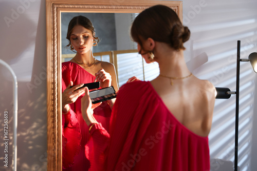 Fotografía Beautiful woman applying makeup while getting ready near mirror indoors