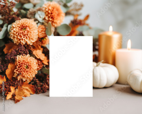 Blank vertical card mockup on the table styled with orange dahlias, golden candles, and white pumpkins