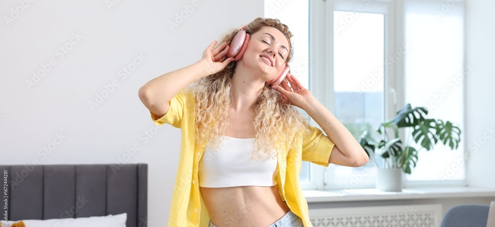 Obraz premium Happy woman in headphones listening to music and dancing at home