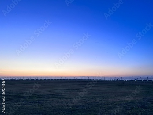 Sunset over golden fields with fence and colorful sky, A golden sunset over a grassy prairie with a rustic wooden fence,  Sunset over a barbed wire fence and rural field, golden light.