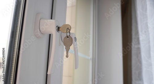 Close-Up of Locked White PVC Window Handle with Two Inserted Keys in Bright Interior with Sheer Curtain, Representing Home Safety, Modern Security, and Window Lock Mechanism Concept