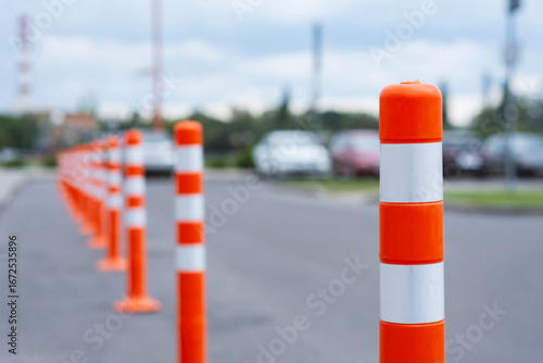 A row of bright orange and white striped traffic cones marking a parking area on a paved road. Roadwork safety barriers.