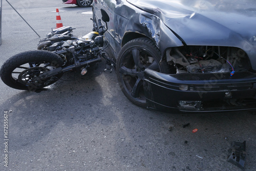 Foto A road accident,a motorcycle lying next to a damaged car with a broken headlight,a warning sign