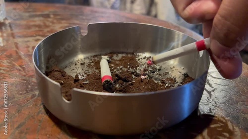 Wallpaper Mural Close-up of a hand tapping ash from a lit cigarette into a stainless steel ashtray on a wooden table Torontodigital.ca