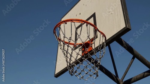 Outdoor basketball court featuring backboard with orange rim and chain net under clear blue sky