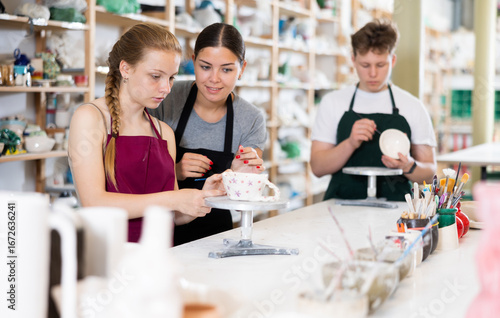 Woman master potter teaches teen girl how to draw and glaze pottery