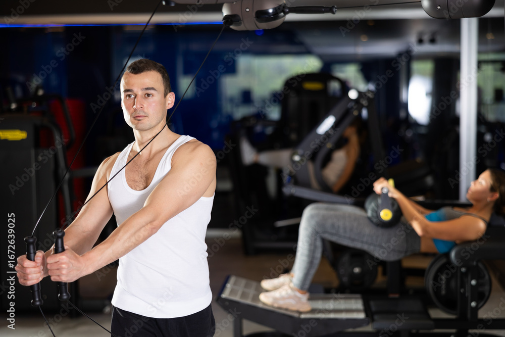 Fototapeta premium Man doing task on loop simulator. He pulls handle with effort. Workout in fitness center, classes to strengthen muscles and create relief. Concept of active and sporty lifestyle