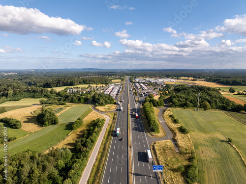 Aerial view of a9 highway near Pegnitz, Bavaria, Germany. Trucks on road amid fields and forests under sunny sky. Shows seamless transport flow