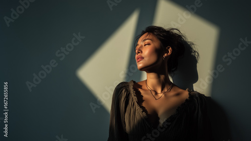 Elegant young woman in dramatic natural light casting geometric shadows on the wall, artistic indoor portrait with cinematic mood, deep shadows, and minimalist composition