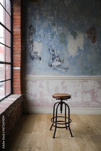 Wooden stool placed against a textured, weathered wall near a window. Perfect for design, interior decor, and minimalist lifestyle concepts.