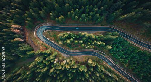 Aerial view of winding mountain road surrounded by dense green forest in the Dolomites, Italy, showing sharp hairpin curves