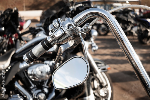 Detail of the chrome handlebar of a motorcycle with lever, electrical controls, and side mirror.