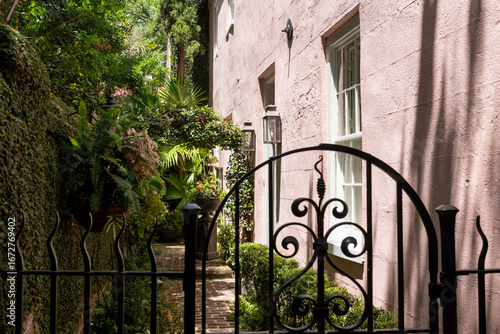 Wrought iron gate opens to a lush courtyard beside a pink stucco home in historic Charleston, South Carolina,