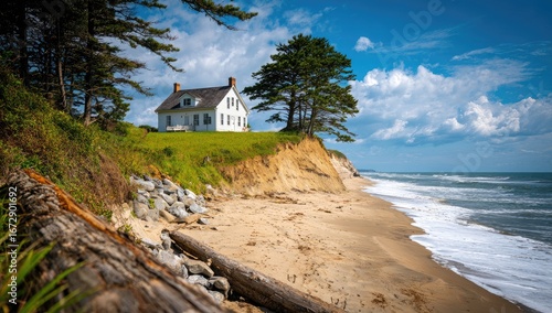A tranquil coastal scene showcasing a weathered white house perched atop a sun-drenched bluff overlooking a sandy beach and placid ocean.