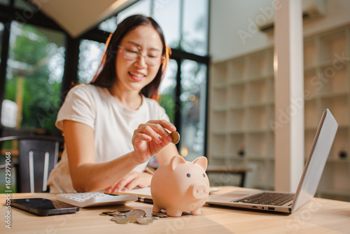 A young Asian woman saves money by putting coins in a pink piggy bank. The concept of saving money.