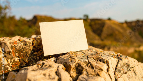 Blank Card in the Wilderness: A pristine blank card rests artfully atop rugged rock, offering space for a message amid the serene beauty of an outdoor landscape.