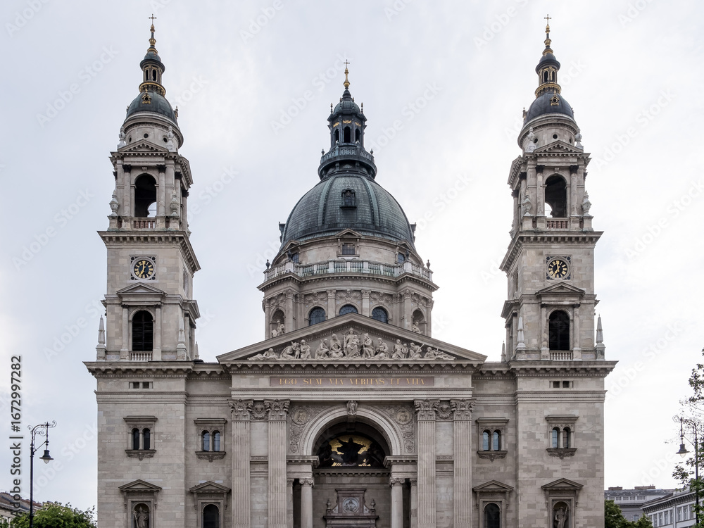 Fototapeta premium Budapest, Hungary – Architectural detail of St. Stephen’s Basilica, showcasing its neoclassical façade, ornate columns, sculpted tympanum, and twin bell towers. A symbol of faith and grandeur.