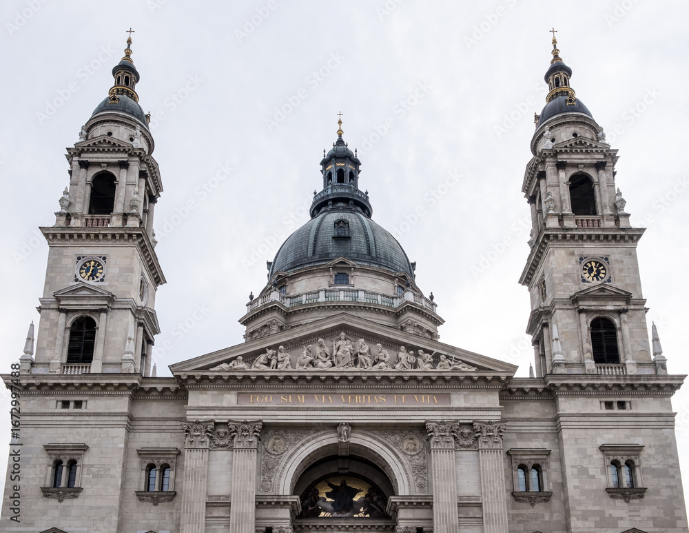Fototapeta premium Budapest, Hungary – Architectural detail of St. Stephen’s Basilica, showcasing its neoclassical façade, ornate columns, sculpted tympanum, and twin bell towers. A symbol of faith and grandeur.