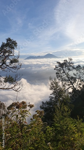 High mountain view with rolling clouds, lush tropical vegetation, and distant peak under clear sky in tranquil nature scene