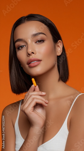 Beauty portrait of a confident woman holding an orange capsule, representing skincare supplements, wellness routines, health balance and modern selfcare.