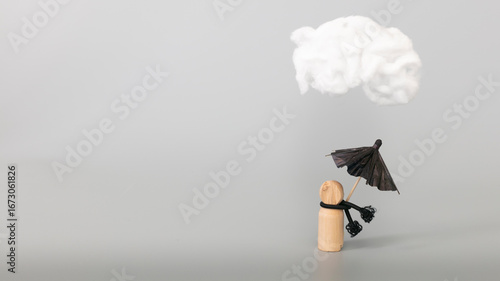 Psychology, solitude, fear or mental health problem concept. Depressed sad person with a cloud overhead, on grey background. Wooden figure with black umbrella symbolize mental health. 