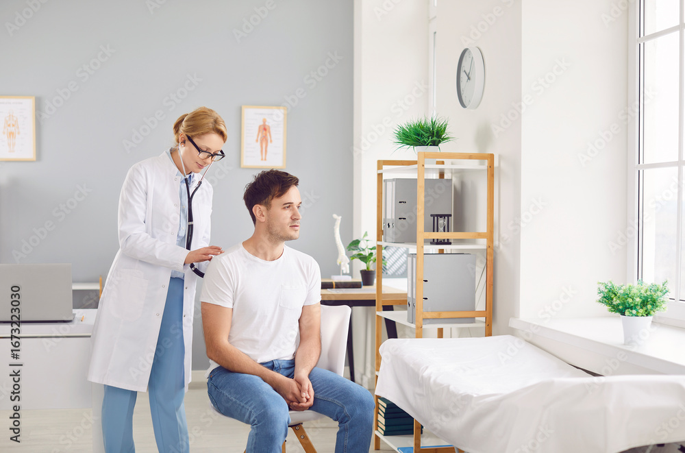 Fototapeta premium Female doctor or nurse using a stethoscope to check the lungs and breathing of a male patient during a hospital checkup. This healthcare visit ensures the patient health and well being.
