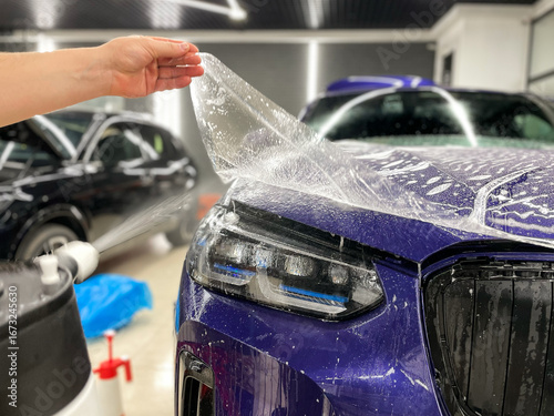 A car wrapping specialist applies a polyurethane film on the front headlight of a car. Car wrapping, detailing, tuning and styling. PPF protective film against chips and scratches. Car protection.