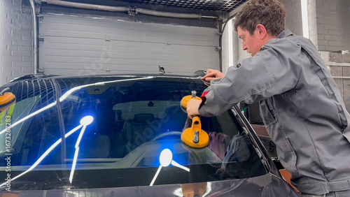 Automobile special workers replacing windscreen or windshield of a car in auto service station garage. Glass of the car, removed with the help of professional suction cups. The process of car repair. 