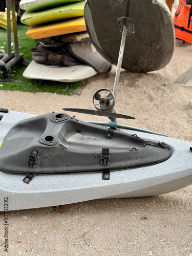 Pedal powered kayak on sandy beach with stacked surfboards and equipment, outdoor water sports scene, adventure and recreation concept