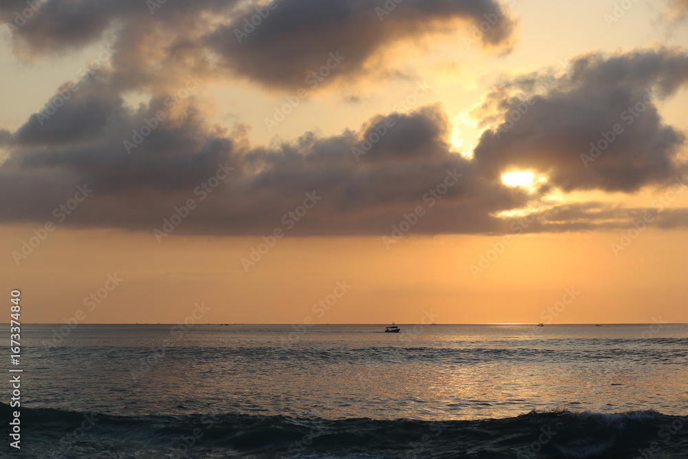 Naklejka premium Ocean panorama with cloudy orange sky and setting sun through the clouds