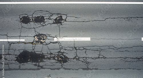Close up aerial view of a damaged asphalt road surface showing cracks potholes and repair patches indicating wear and tear on infrastructure