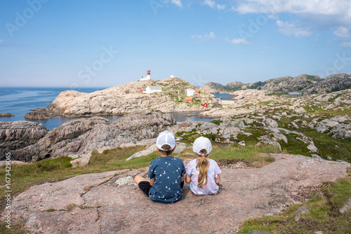 Two small children sitting on a rock looking at the Lindesnes Lighthouse. Lindesnes Fyr on most southern point of Norway, Europe. 
