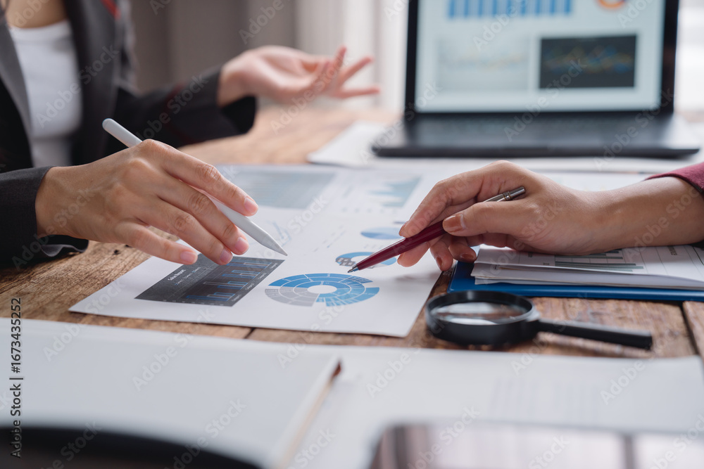 Fototapeta premium Businesswomen are analyzing financial charts and graphs using magnifying glass and pens during a meeting to discuss investment strategy and business performance