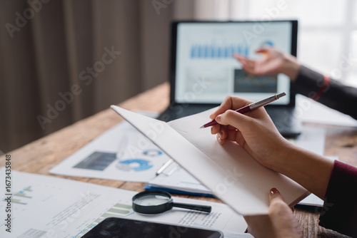 Photography Businesswomen taking notes while analyzing financial charts displayed on a lapto