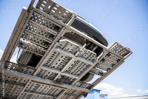 Visible chassis and bottom of pre-owned car on upper car hauler platform, white wagon on car carrier trailer, car-carrying, hauler, auto transport trailer, semi-trailer with hydraulic piston.