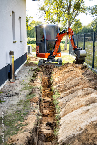 Mini excavator digging a trench next to a single family house