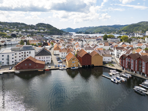 Aerial view of a tranquil town where waters meet colorful buildings under a vast sky, a captivating blend of nature and architecture, Flekkefjord, Agder, Norway.