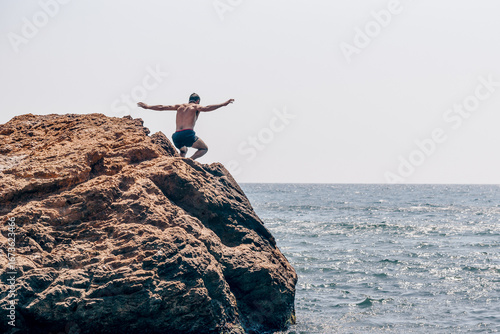 Canvas Print Man in swimsuit jump from large stone cobblestone into water pond sea on summer